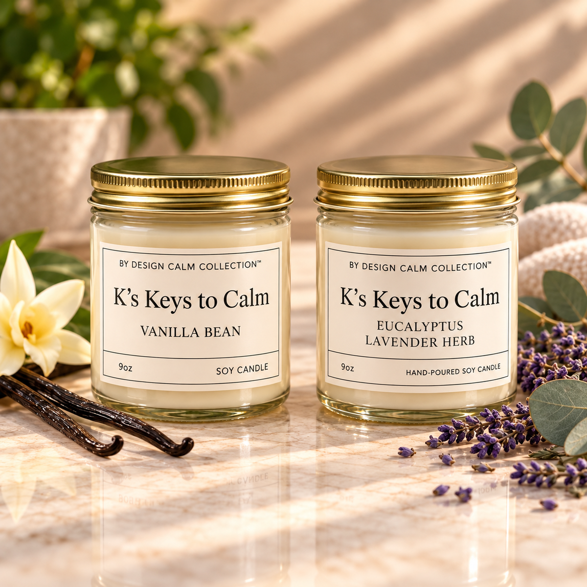 Two 9oz soy candles by Design Calm Collection, 'K's Keys to Calm', in clear glass jars with gold lids, displayed on a marble surface with vanilla beans, lavender, and flowers.