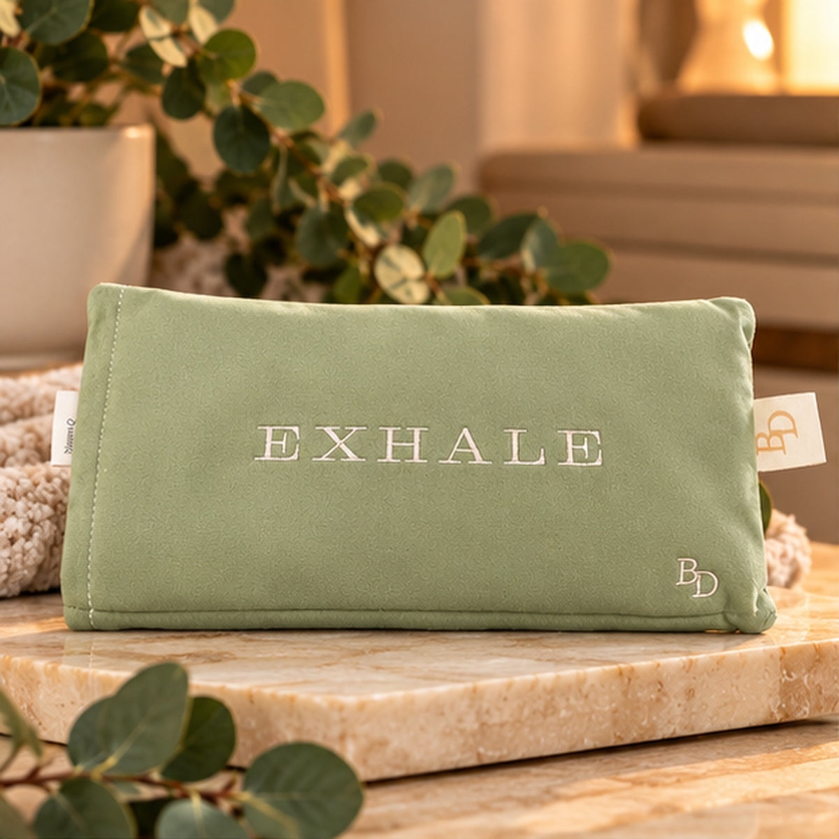 Sage EXHALE Weighted Eye Pillow displayed on a stone tray with warm neutral styling and greenery.