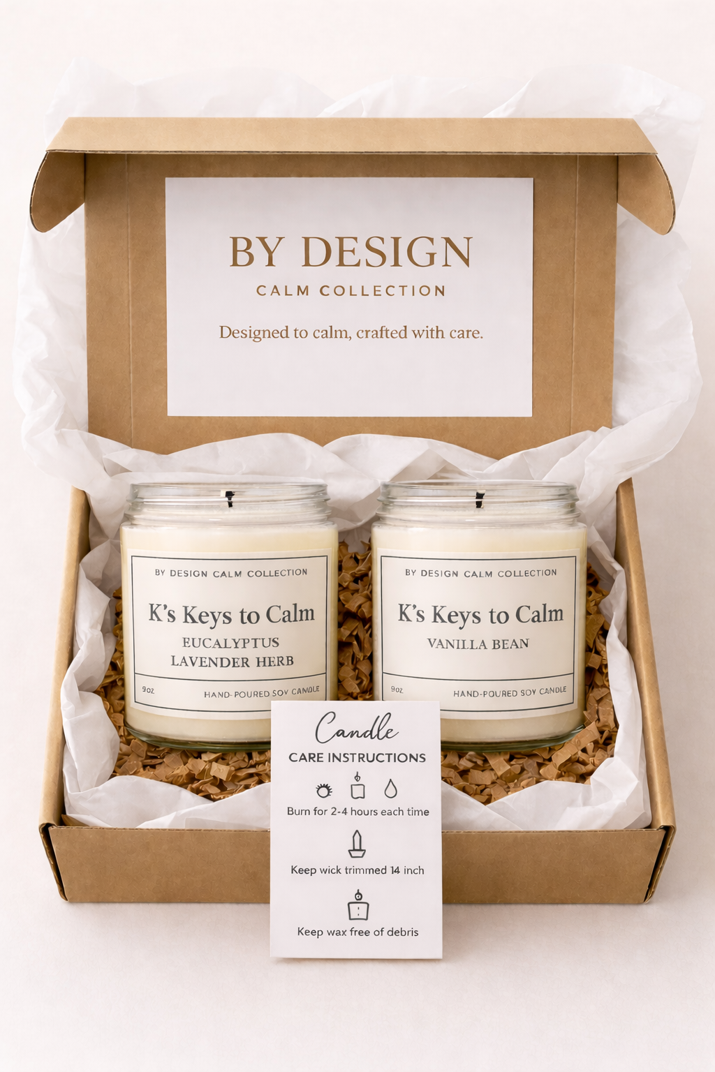 Two candles in a 'By Design' gift box with a card on a white background