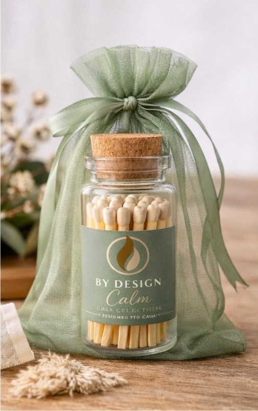 Jar of matches with a green bow and 'By Design Calm' label on a wooden surface.