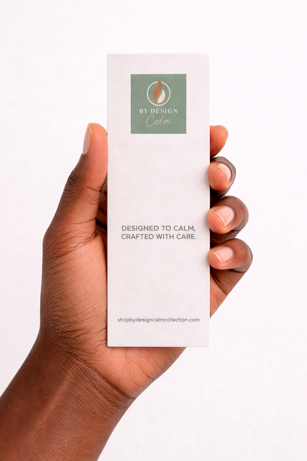 Hand holding a small white box with 'By Design' branding on a light background