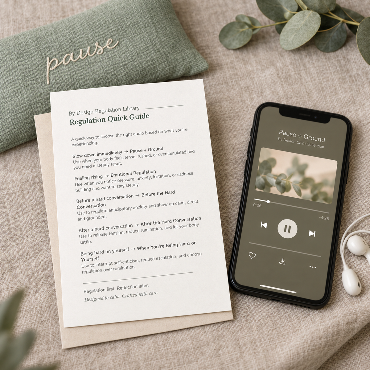 A styled flat-lay showing a printed 'pause' Regulation Library quick guide card next to a smartphone displaying a music player with a pause icon, on a textured beige fabric background with eucalyptus leaves.