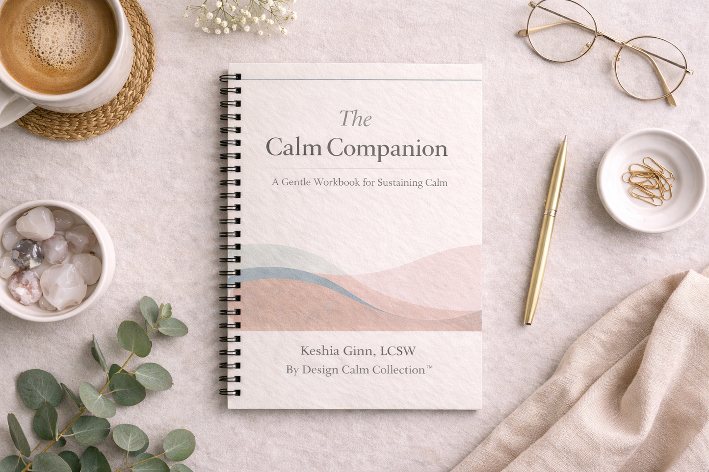 Spiral-bound book titled 'The Calm Companion' on a light surface with a cup of coffee, glasses, and eucalyptus leaves.
